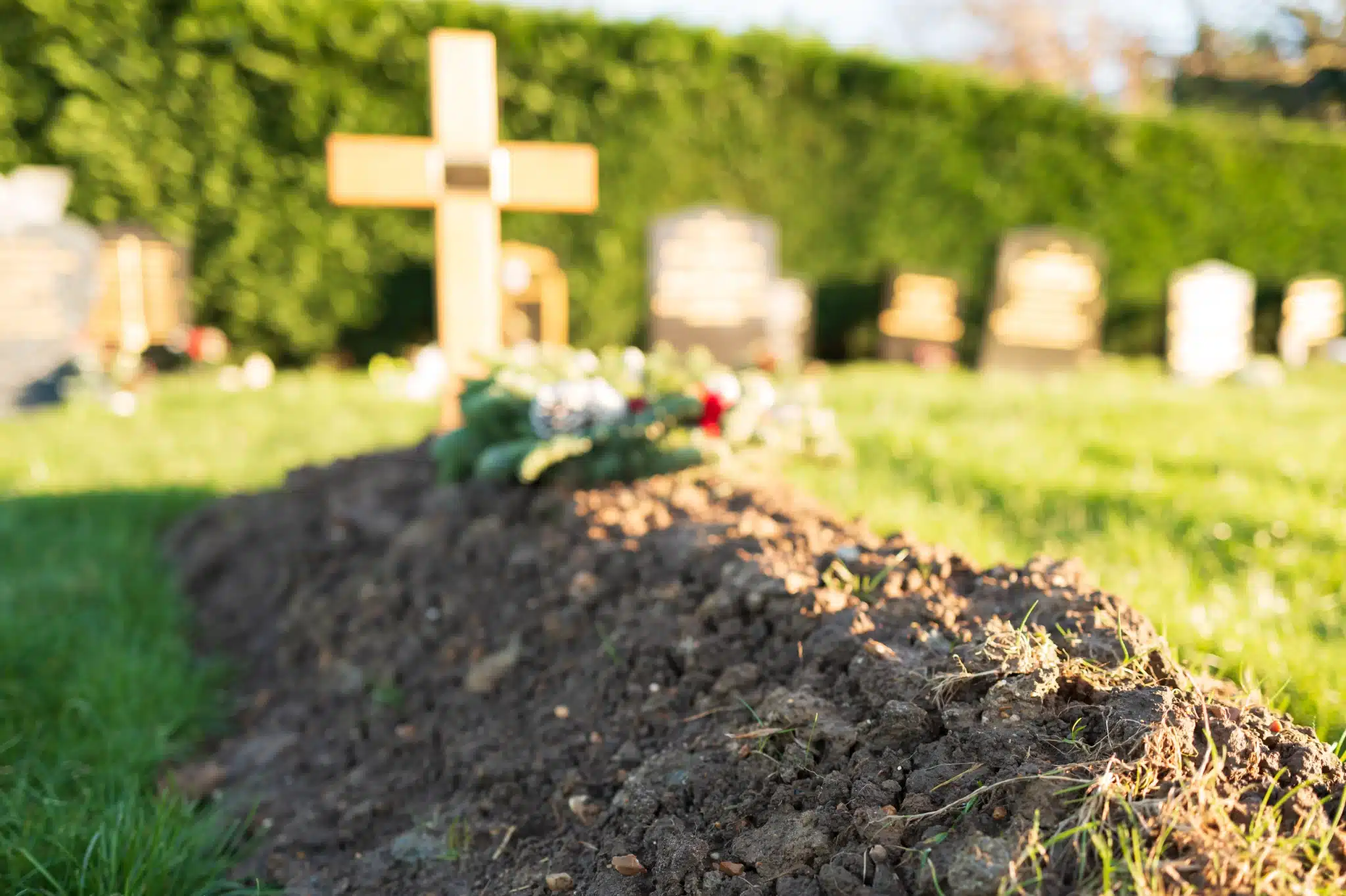 Fresh grave with cross and flowers in cemetery for green burial services in Laguna beach california