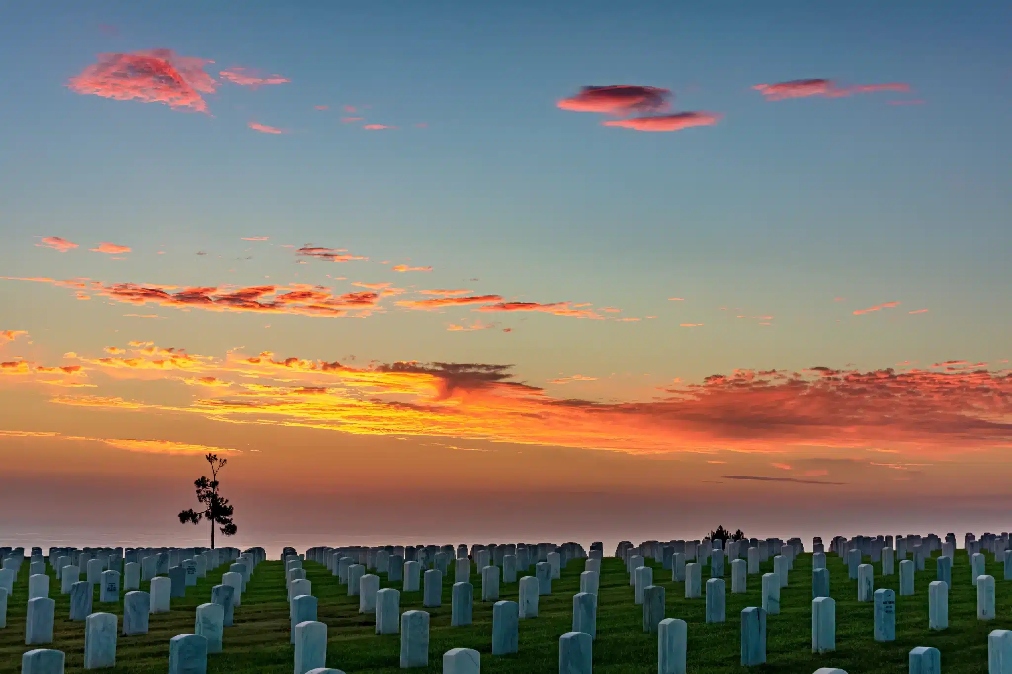 Sunset over cemetery with vibrant clouds and silhouetted tree for Green Burial Services in San Mateo County, California