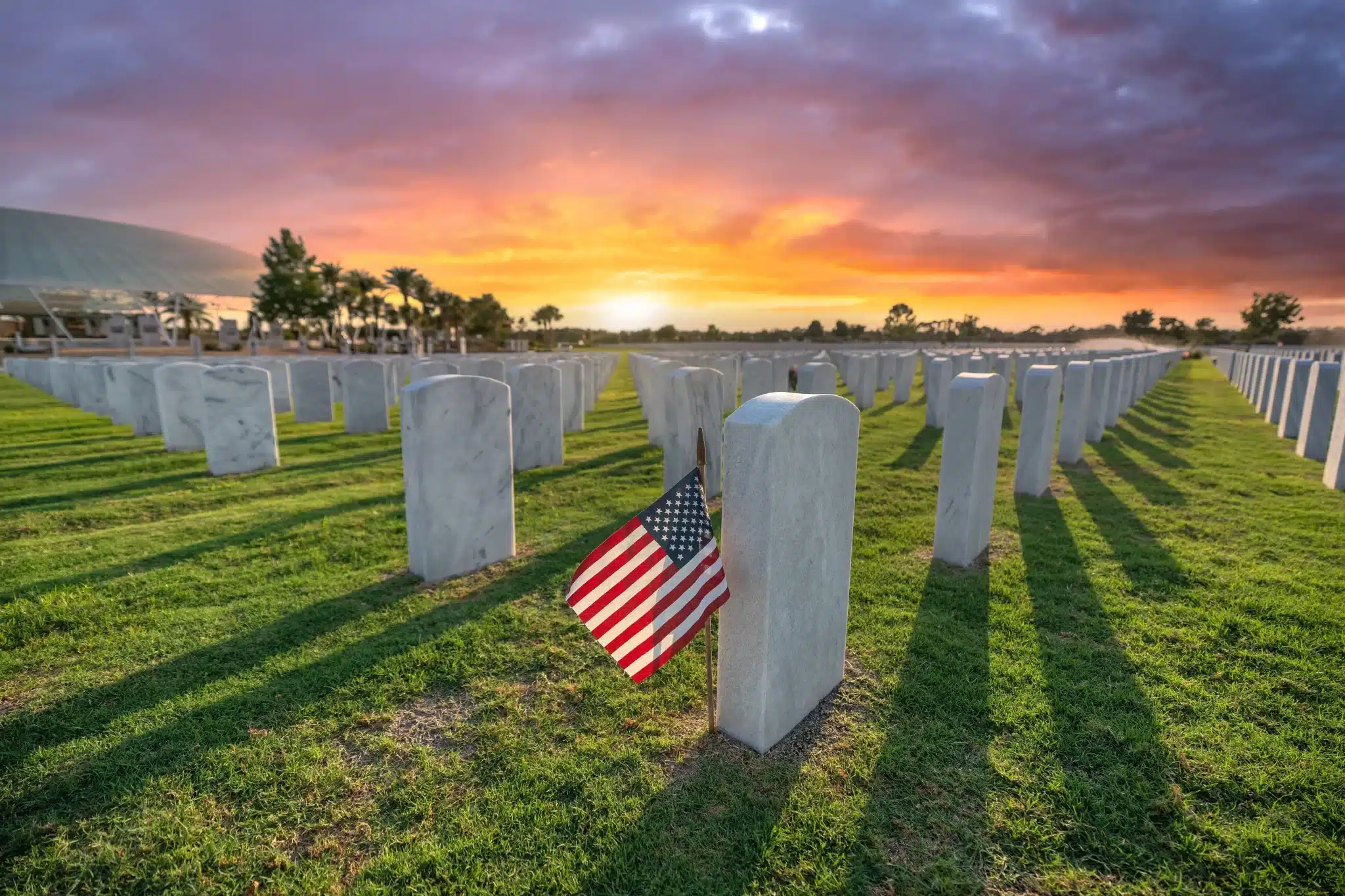 Sunset at American cemetery with flag-adorned tombstone for Green Burial Services in Newport Coast, California